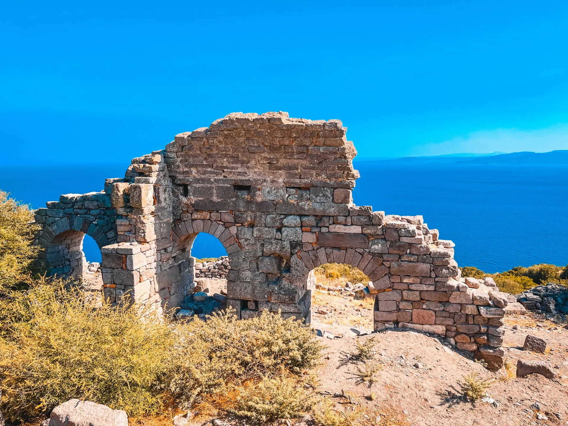 Çanakkale Assos'taki antik kentin taş kemerli kalıntıları, arkasında Ege Denizi'nin masmavi manzarası.